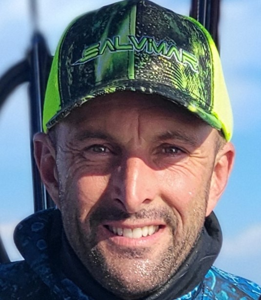 Rudy Levy souriant sur un bateau, casquette vissée sur la tête, sous le soleil